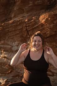 Smiling person with short black hair in a blue shirt, in front of green plants.