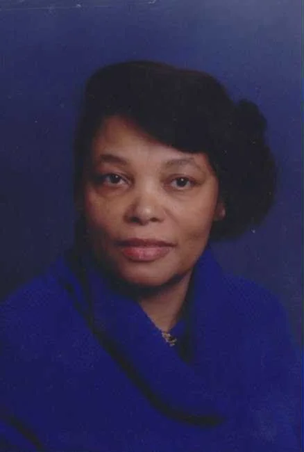 A portrait of a woman with short dark hair, wearing a blue top, set against a dark background.
