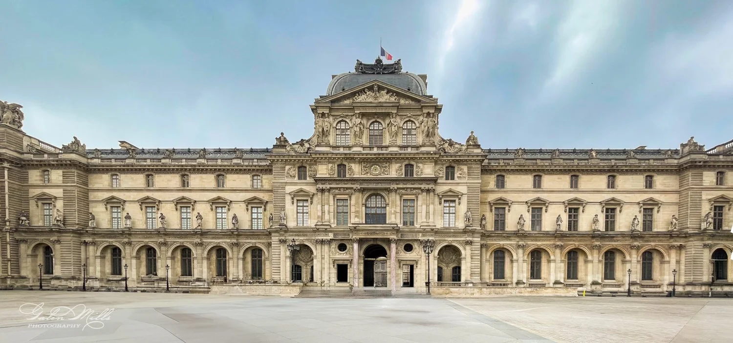 Facade of the Louvre Museum in Paris with a French flag on top.