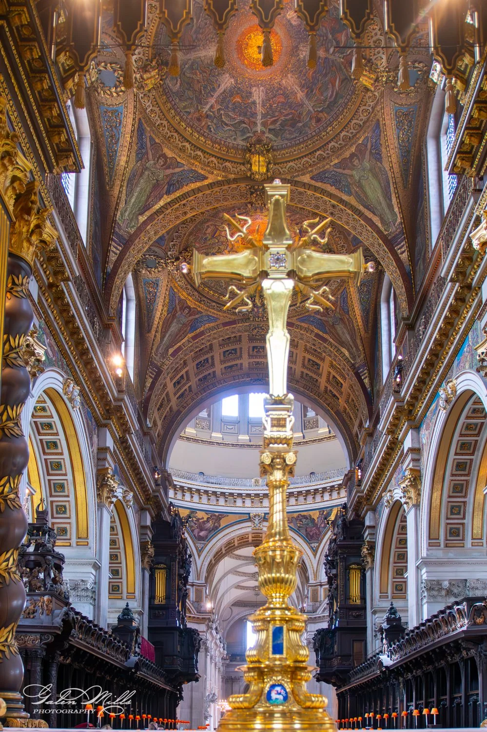 Interior of a cathedral with a golden cross in the foreground and ornate ceilings.