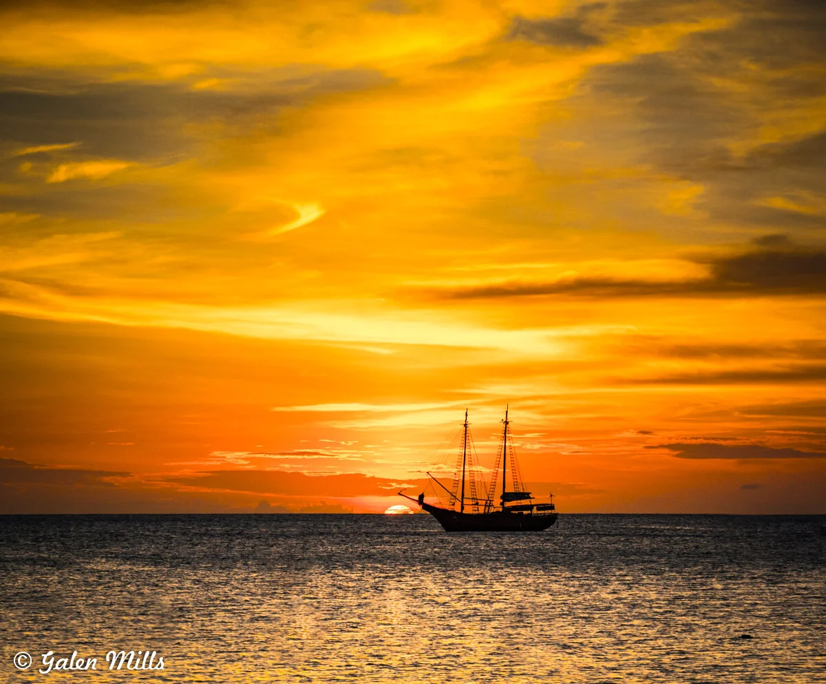 Sailboat silhouette against a vibrant yellow and orange sunset over the ocean.