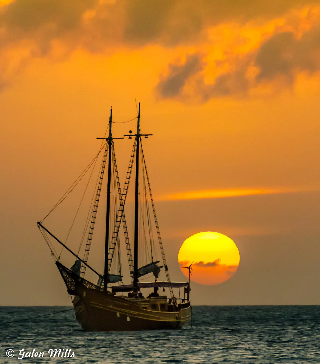 Sailing ship at sea with sunset in the background, orange sky.