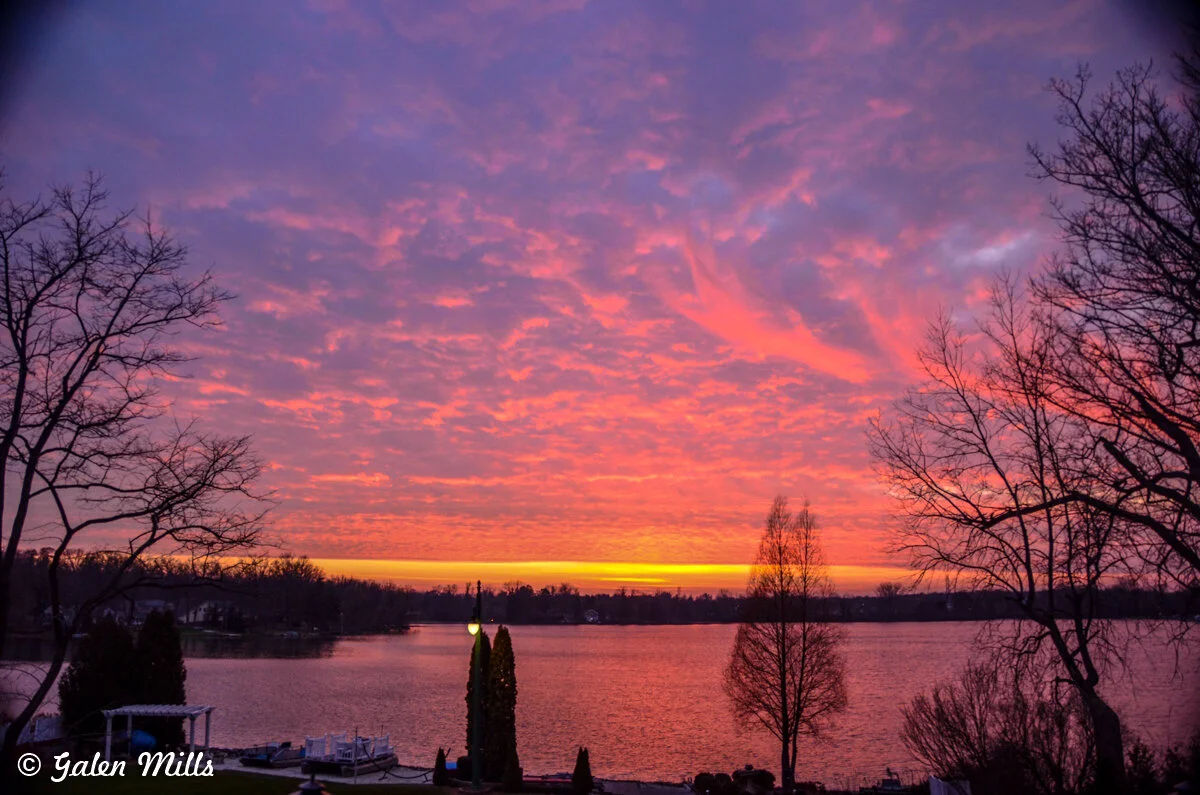 Colorful sunset over a lake with silhouetted trees and vibrant clouds.