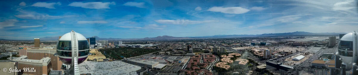 Panoramic view of Las Vegas with High Roller observation wheel and cityscape under a blue sky.
