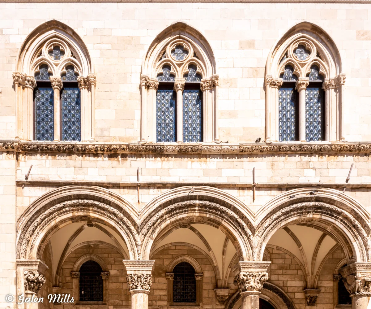 Close-up of arched windows and archways in a historic stone building facade, featuring Gothic architectural details.