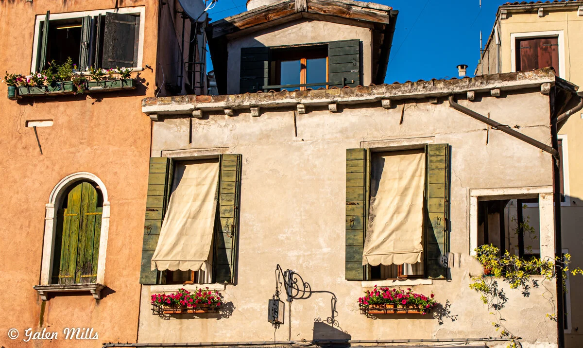 Traditional Italian building with wooden shutters, flower boxes, and stucco facade in warm sunlight