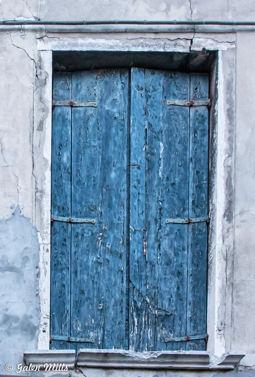 Weathered blue wooden window shutters on a concrete wall.