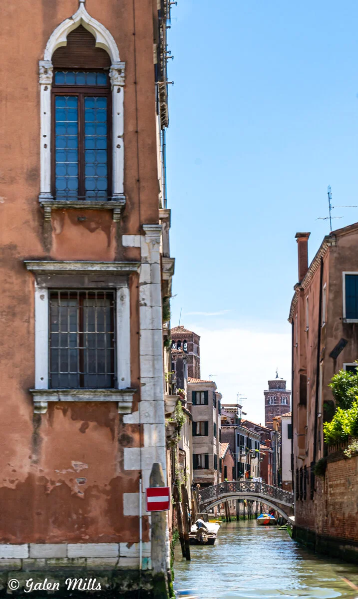 Venetian canal with arched bridge, historic buildings, and clear blue sky