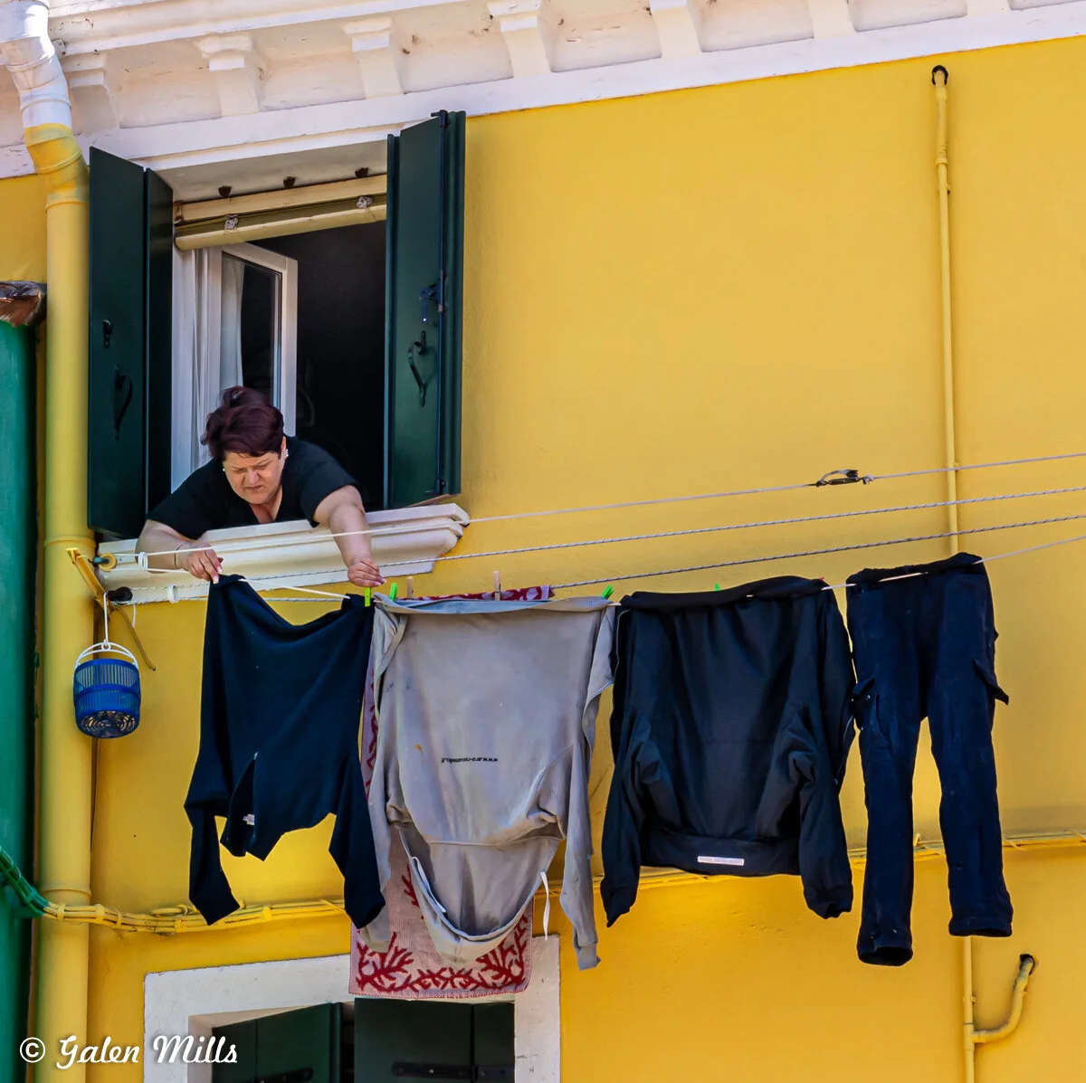 Person hanging clothes on a clothesline outside a yellow building.