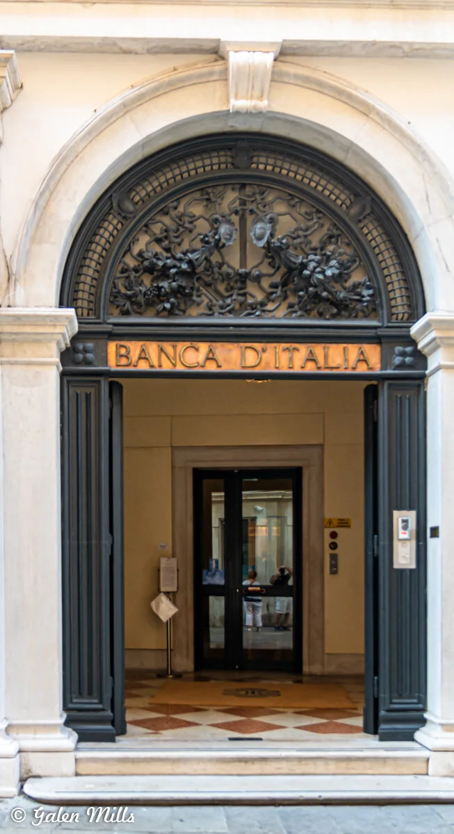 Entrance of Banca d'Italia building with ornate arch and open door.