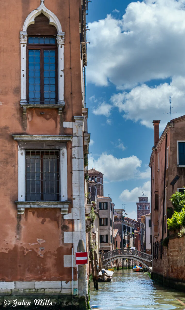 Venetian canal with a bridge, old buildings, and a blue sky with clouds.