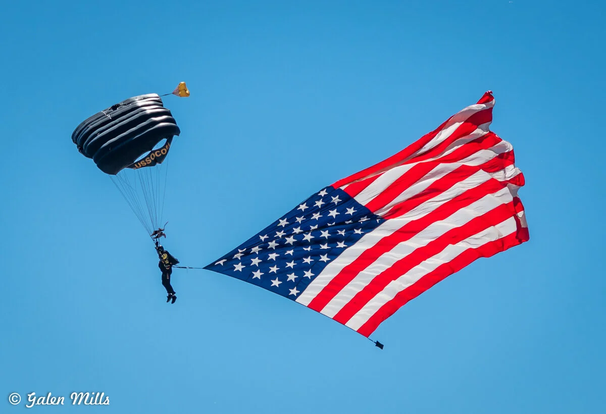Parachutist descending with American flag in clear blue sky.