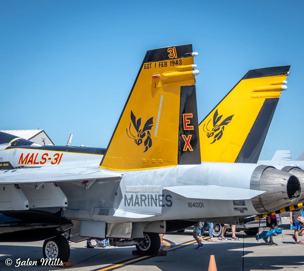 Two military fighter jets on display with yellow and black tail markings, showing a stylized hornet design and "MALS-31" text. The word "MARINES" is visible on the aircraft body.