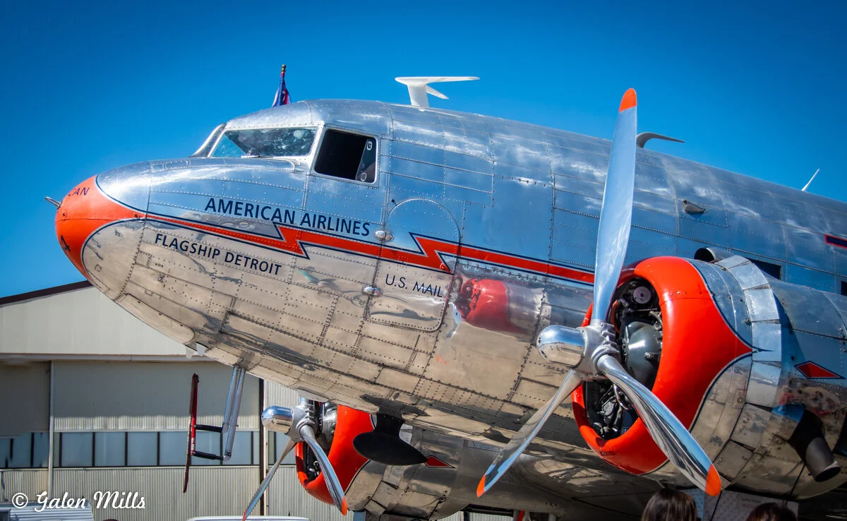 Close-up of a vintage American Airlines plane named Flagship Detroit with polished metal fuselage and red accents, at an airfield.