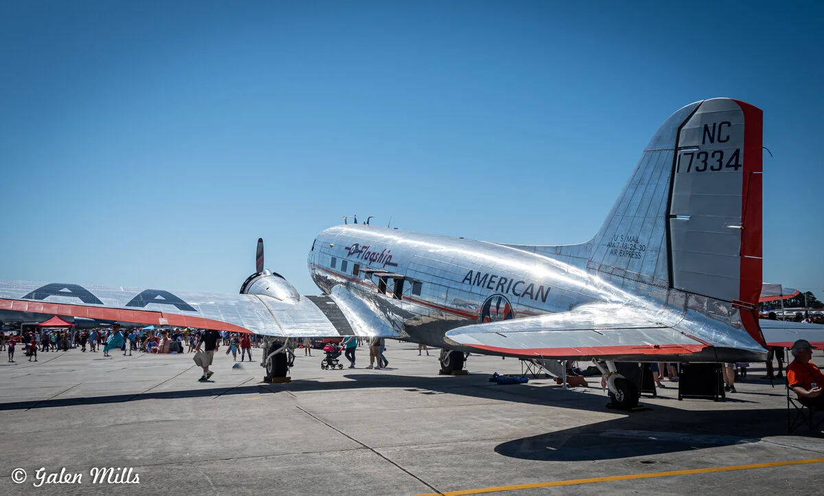 Vintage American Airlines aircraft parked on an airfield with people around it under clear blue sky.