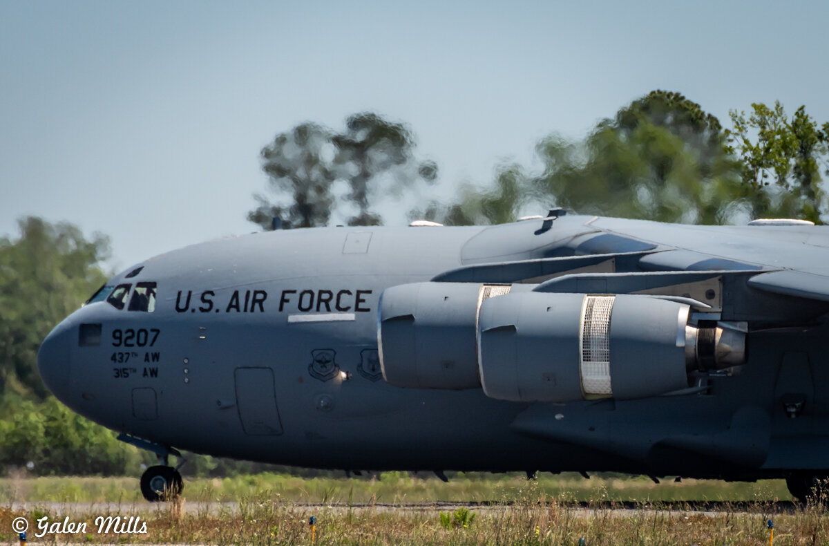 U.S. Air Force C-17 Globemaster III on an airstrip with trees in the background.