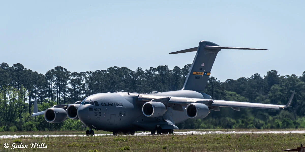 A U.S. Air Force C-17 Globemaster III aircraft on a runway with trees in the background.