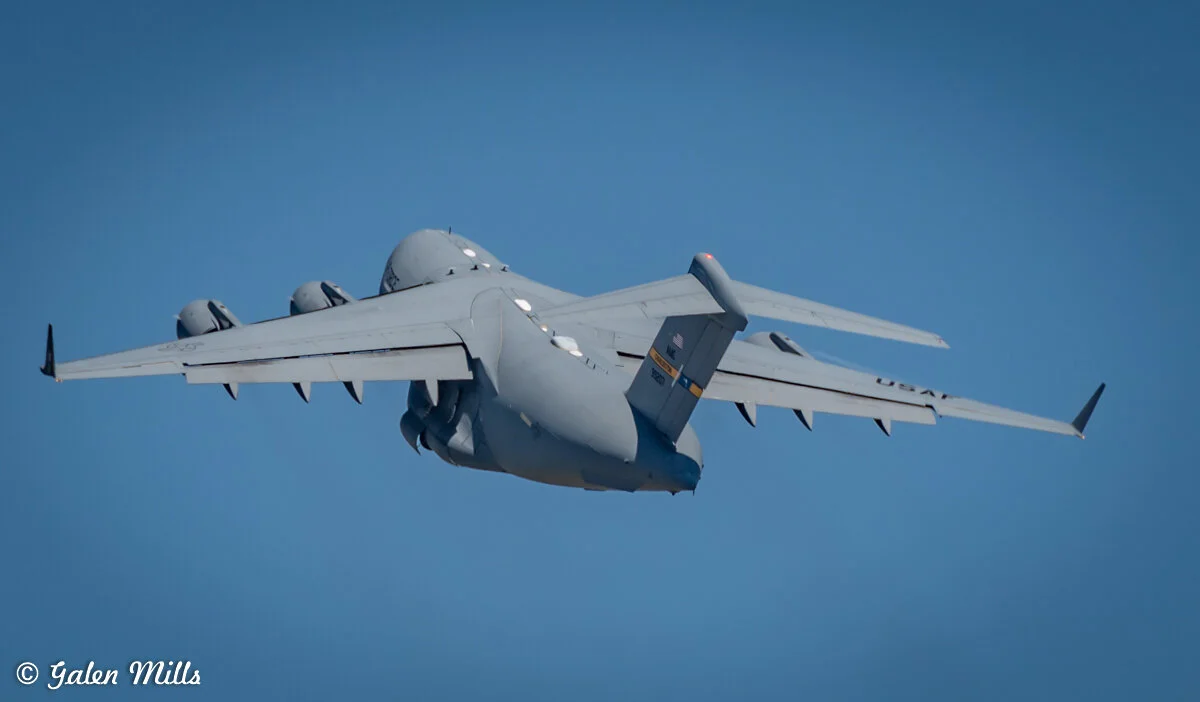 A large military cargo plane in flight with a clear blue sky background.
