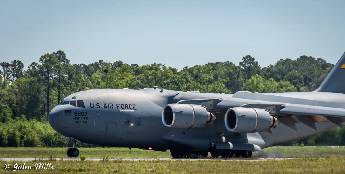 A U.S. Air Force C-17 Globemaster III aircraft taxiing on a runway with a green forest in the background.