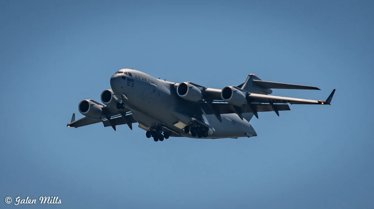 A U.S. Air Force C-17 Globemaster III aircraft in flight against a clear blue sky.