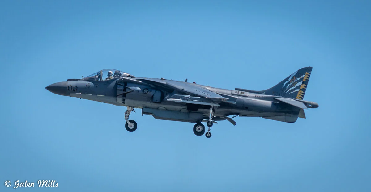 A fighter jet in flight with landing gear extended on a clear blue sky background.