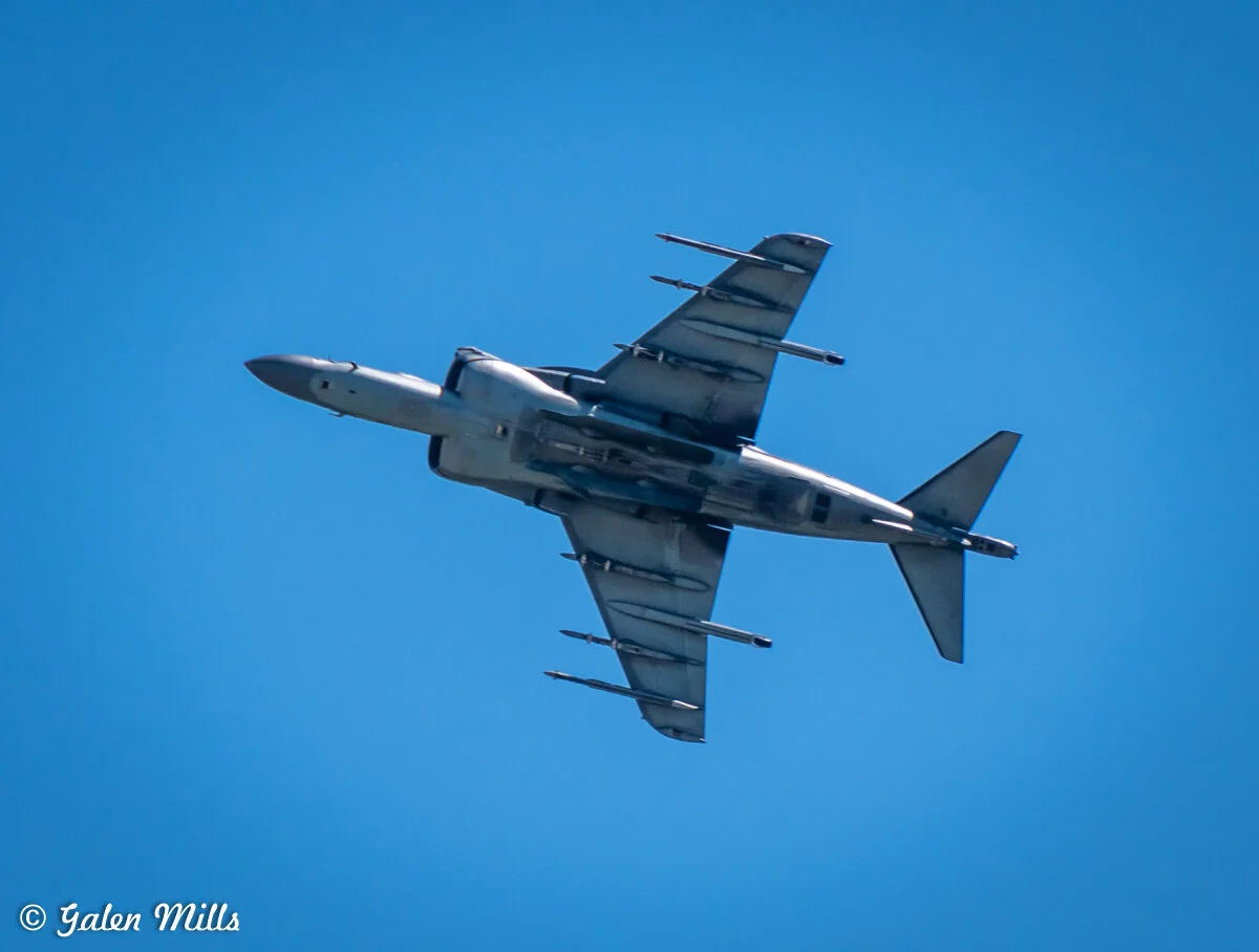 Military jet flying overhead against a clear blue sky.