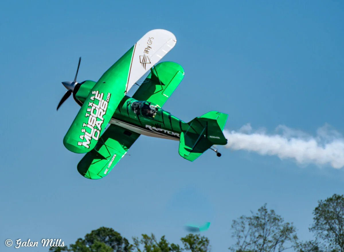 Aerobatic biplane performing stunts in the sky with smoke trail, blue sky background.
