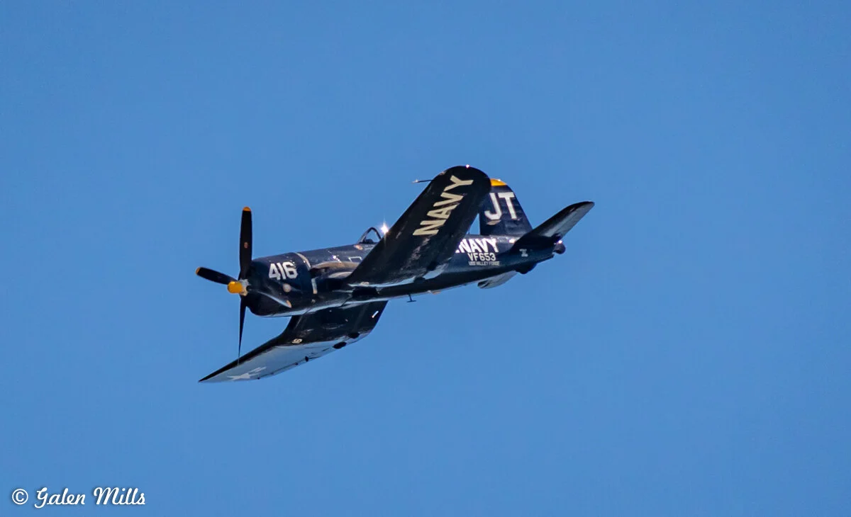 Vintage Navy airplane in flight with "416" and "NAVY" markings on a clear blue sky background.