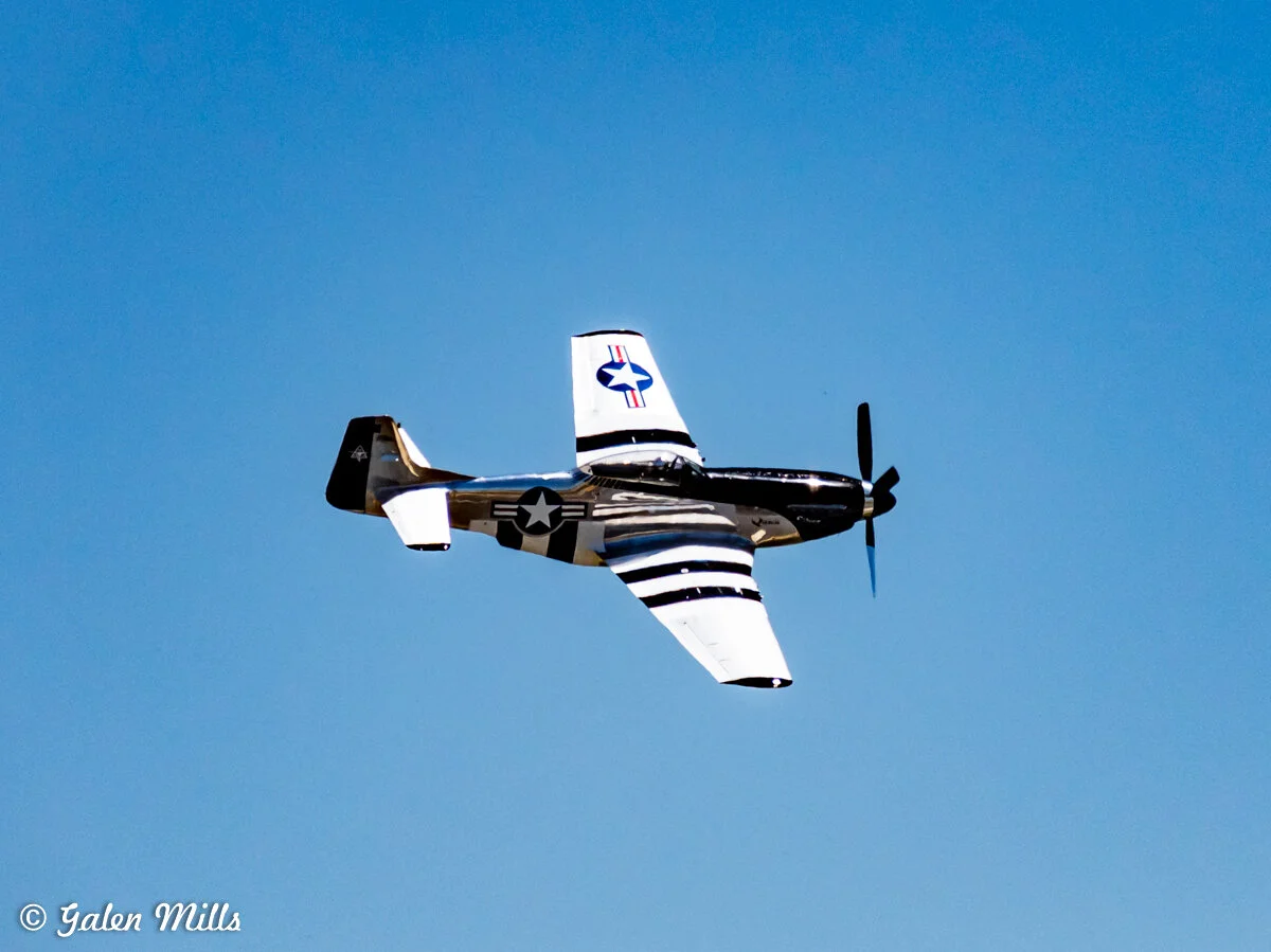 WWII-era P-51 Mustang fighter plane in flight against clear blue sky.