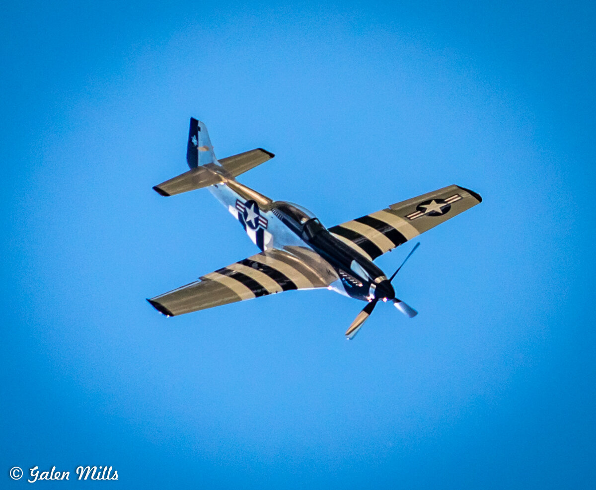 World War II-era fighter plane with US Air Force insignia flying in clear blue sky.
