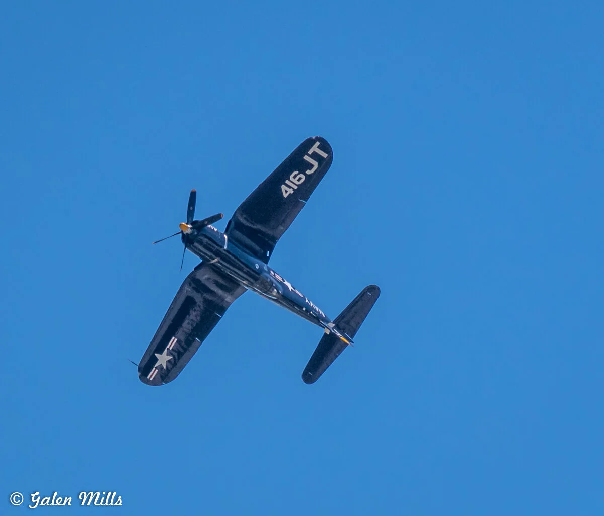 Vintage military aircraft in flight with "416 JT" on the wing, under a clear blue sky.