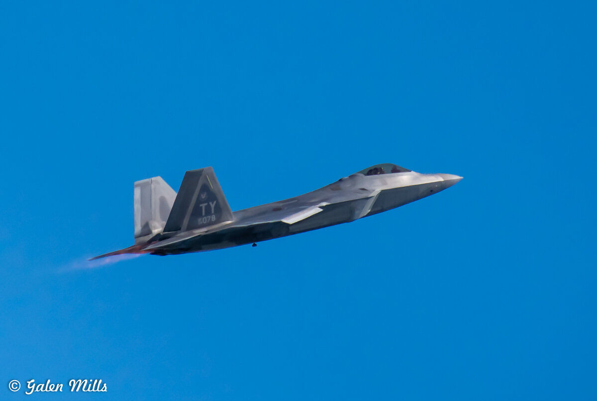 F-22 Raptor fighter jet flying in a clear blue sky.