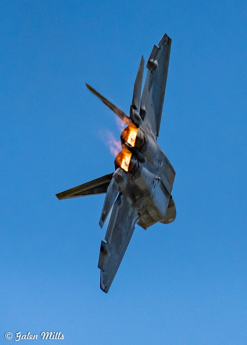 Jet fighter in flight with afterburners on, blue sky background.