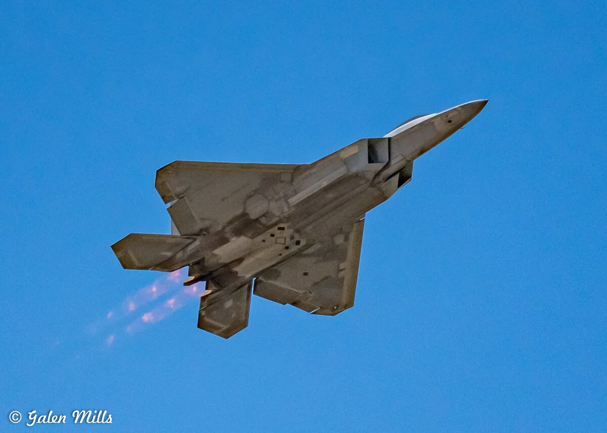 Fighter jet flying with afterburners engaged, clear blue sky background.
