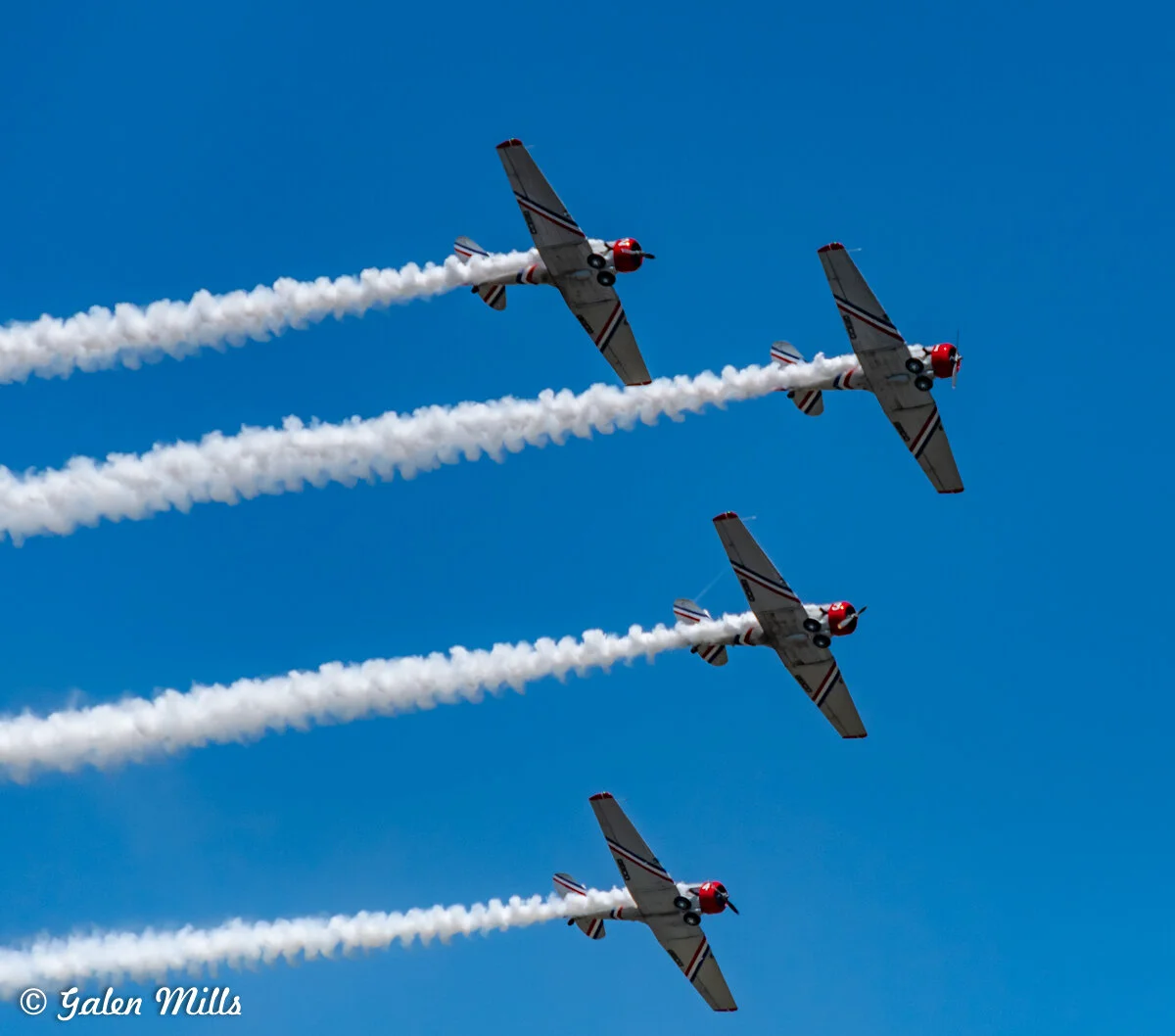 Four aircraft flying in formation, leaving smoke trails against a clear blue sky.