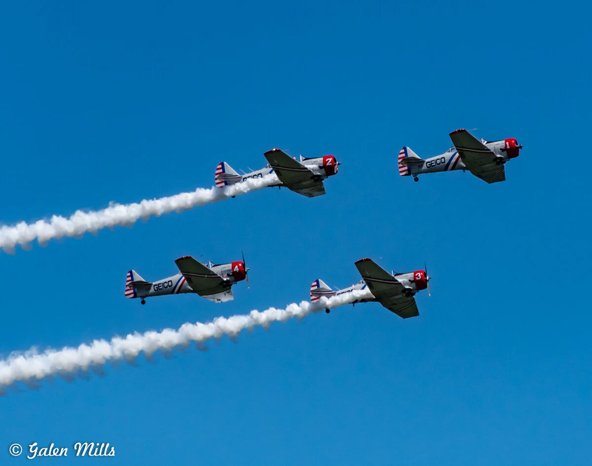 Four vintage airplanes in formation emitting smoke trails
