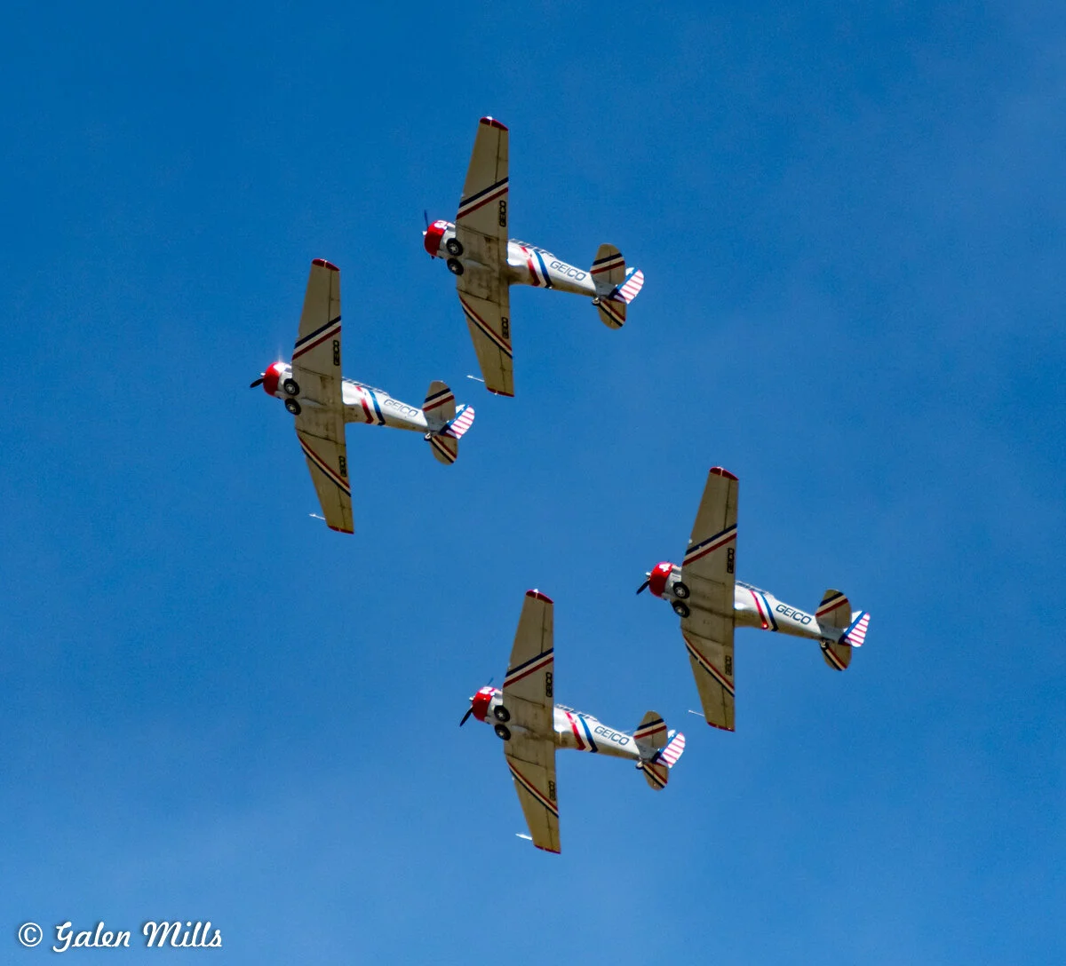 Four vintage military trainer planes performing an aerial formation against a clear blue sky.