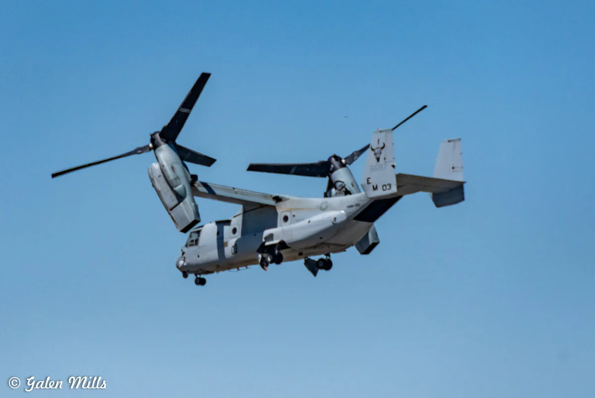 Tiltrotor aircraft flying in clear blue sky.