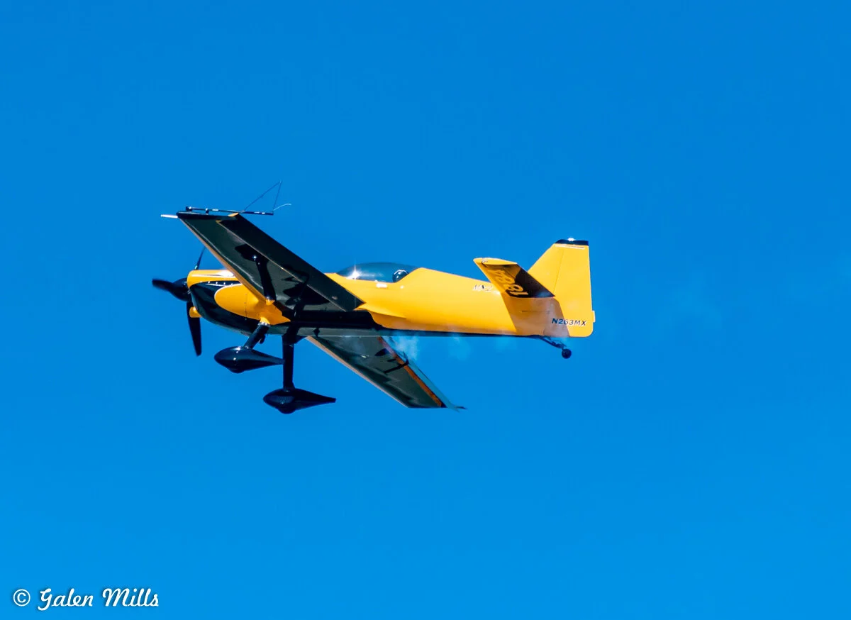 Yellow aerobatic plane flying in clear blue sky