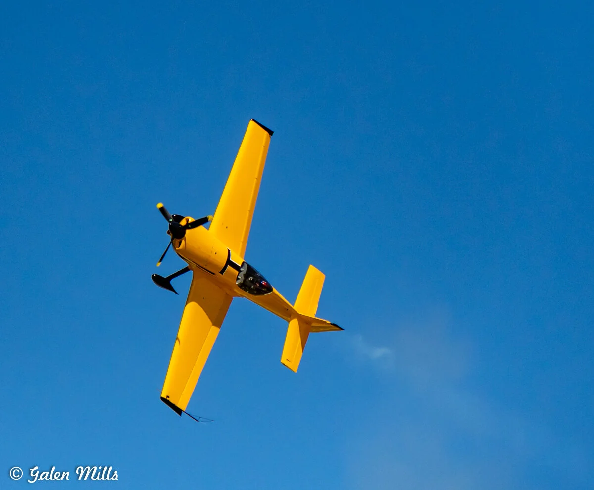 Yellow aerobatic airplane performing a roll in clear blue sky