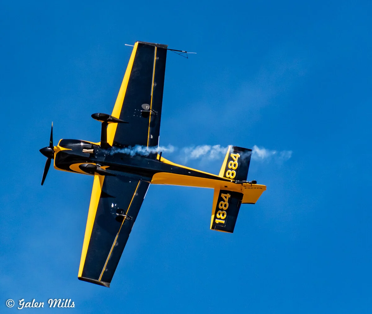 Yellow and black aerobatic airplane in flight against clear blue sky.