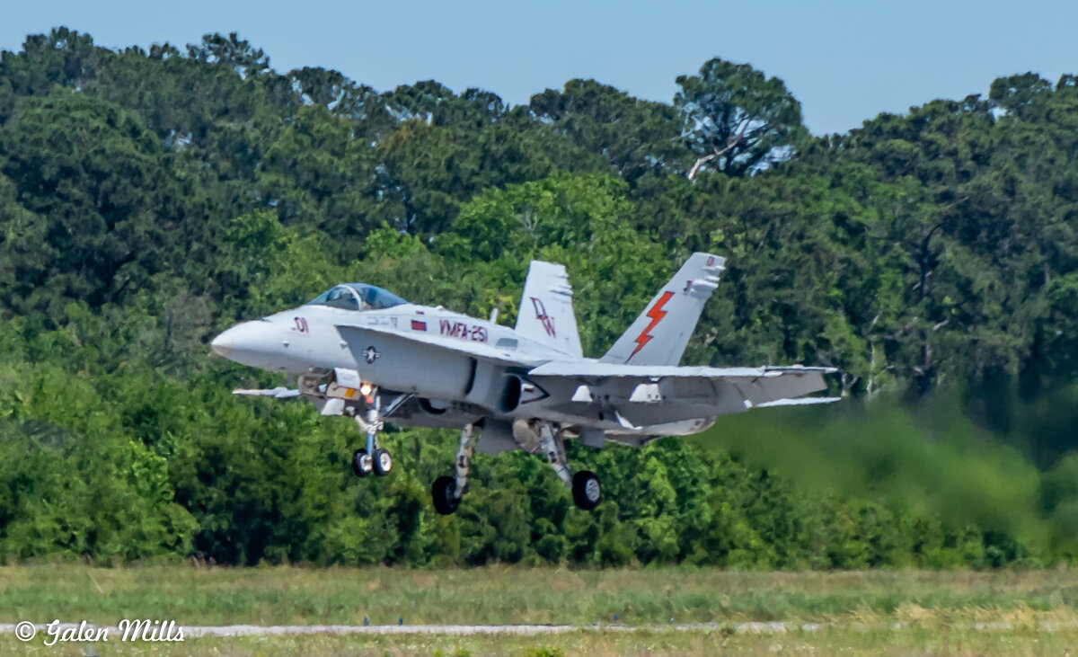 F/A-18 Hornet fighter jet landing on an airstrip with trees in the background.