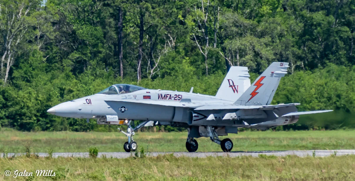 Military jet aircraft parked on a runway with a forested background.