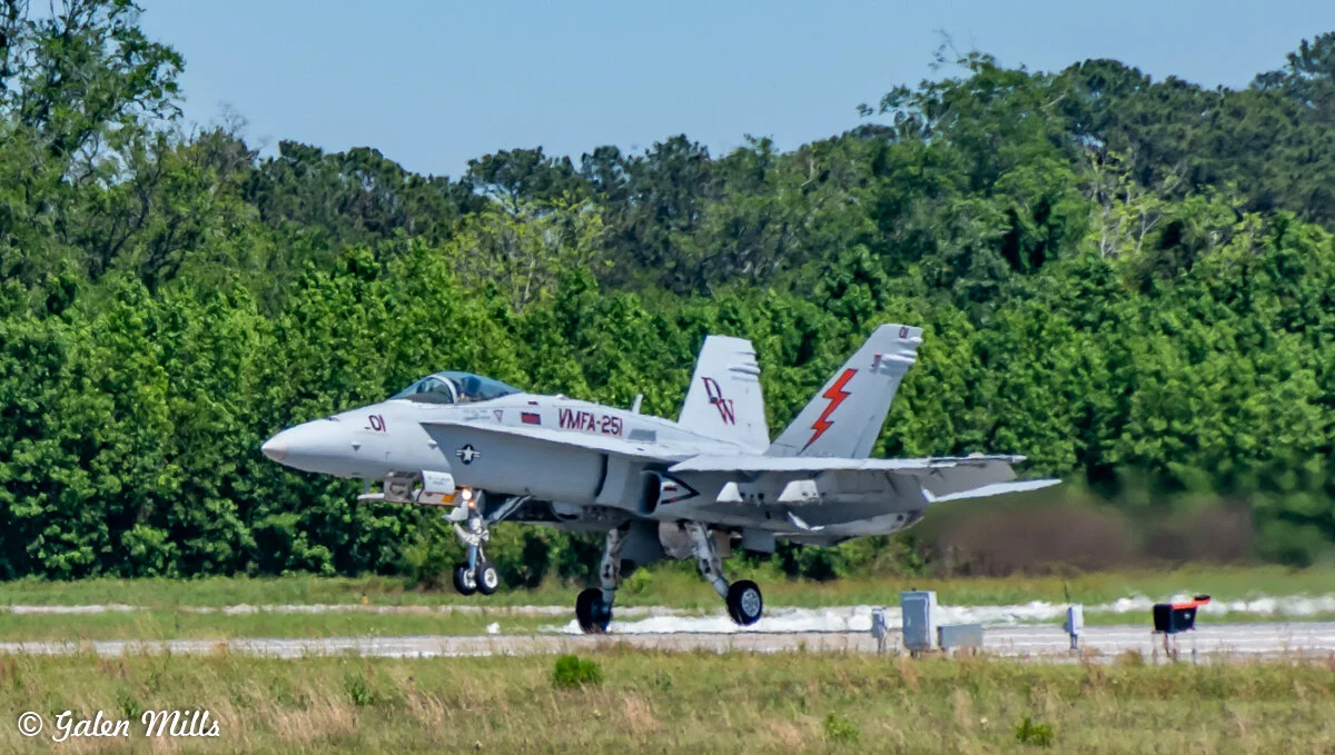 F/A-18 Hornet fighter jet landing on a runway with trees in the background.