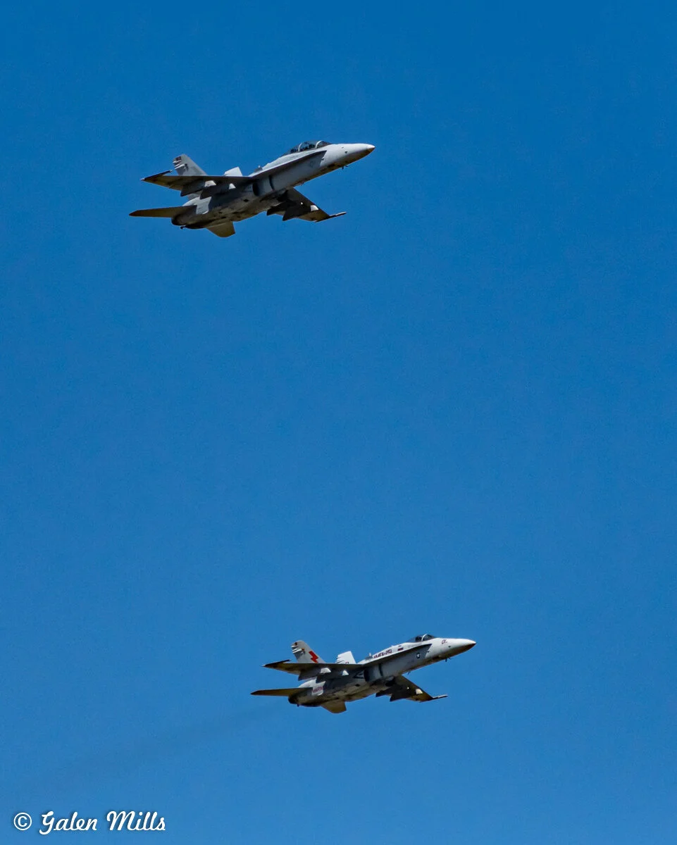 Two military fighter jets flying in formation against a clear blue sky.