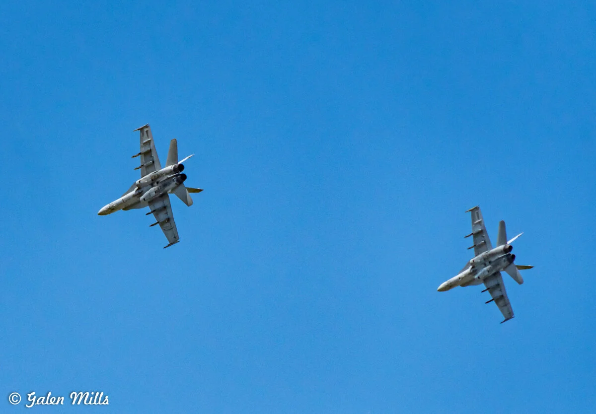 Two military fighter jets flying in formation against a clear blue sky.
