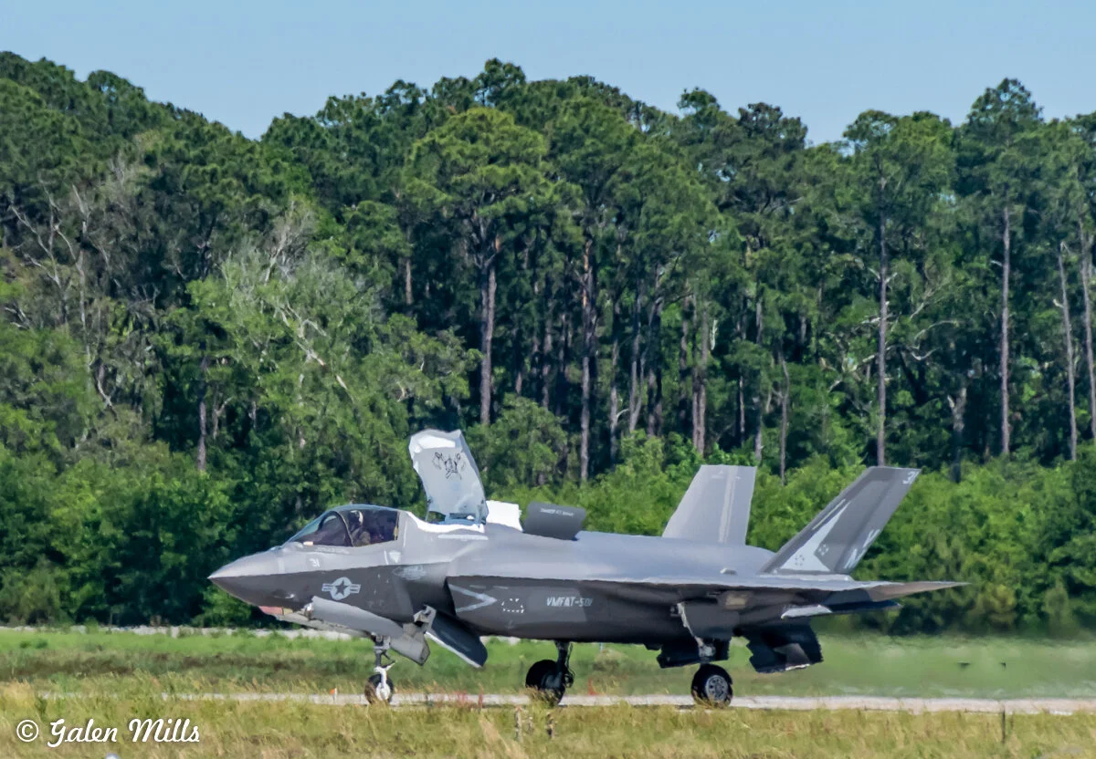 A gray fighter jet parked on a runway with dense green forest in the background.