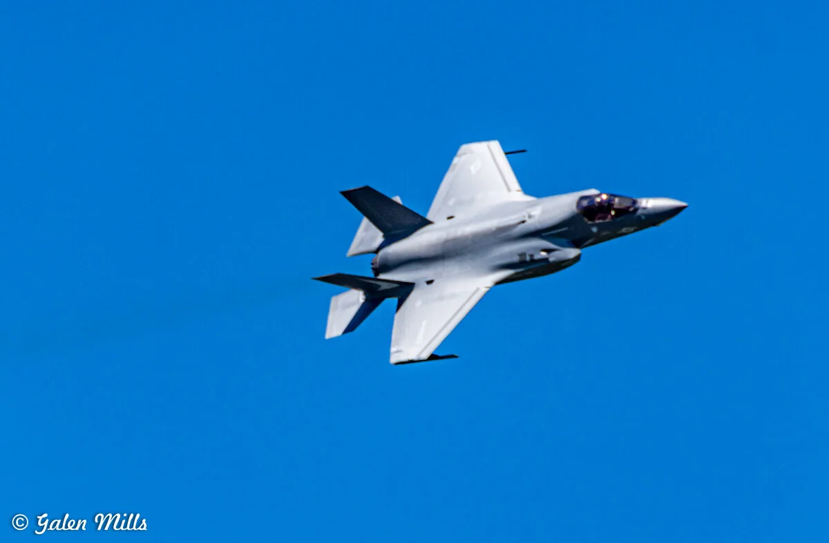 A military fighter jet flying against a clear blue sky.