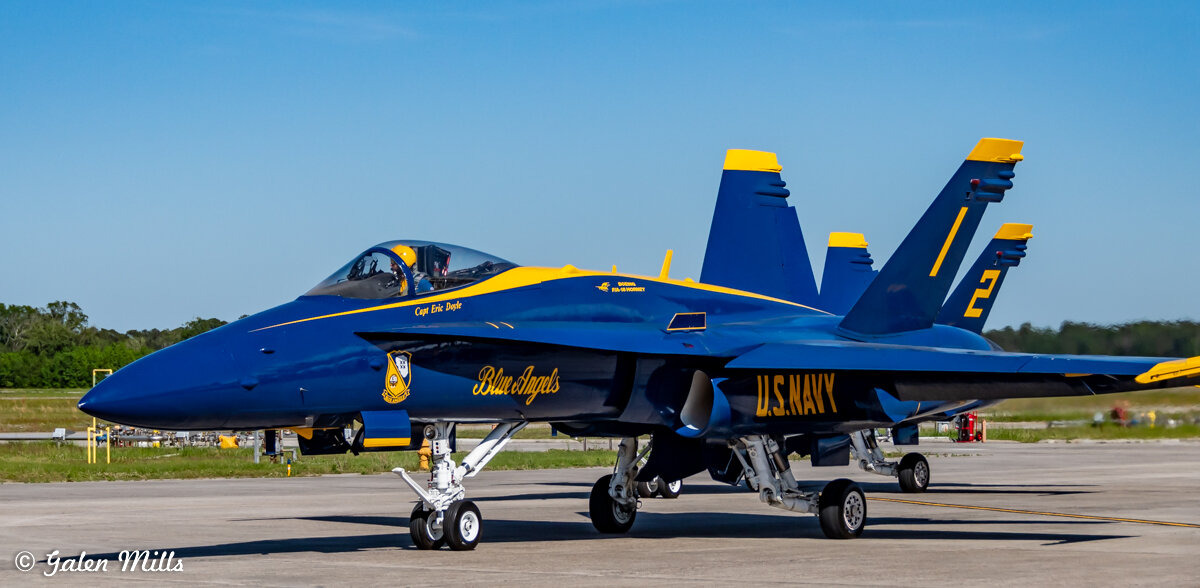 Blue Angels F/A-18 Hornet jet on tarmac, blue and yellow colors, marked "U.S. Navy" and "Blue Angels."