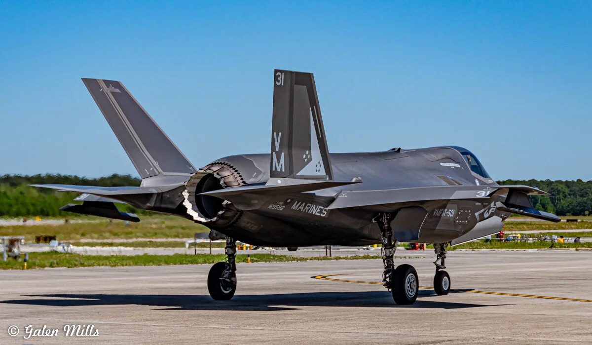 F-35 fighter jet on an airstrip, marked with 'Marines' and military insignia, against a clear blue sky.